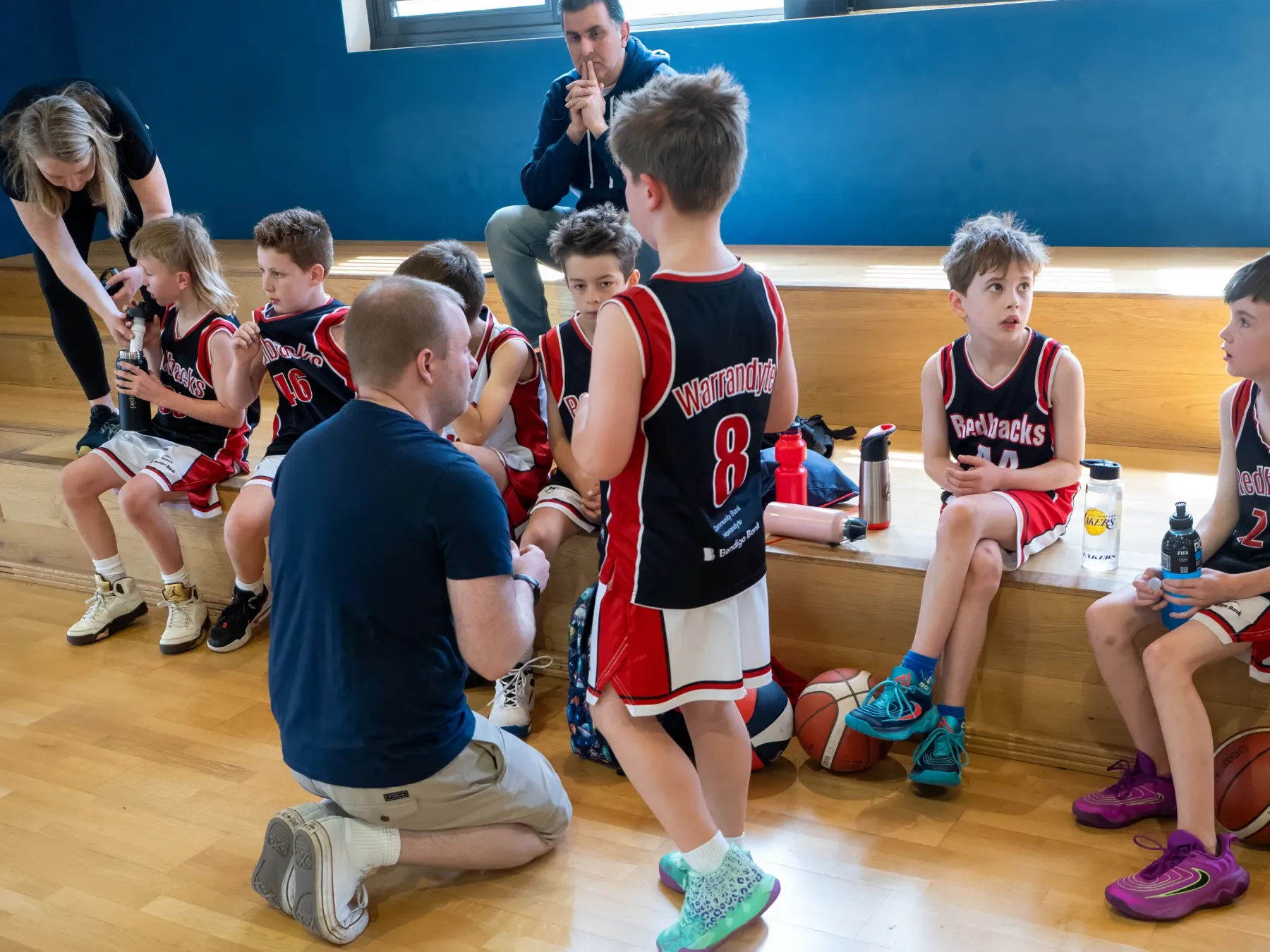 A Redbacks coach kneeling to talk to the team on the bench