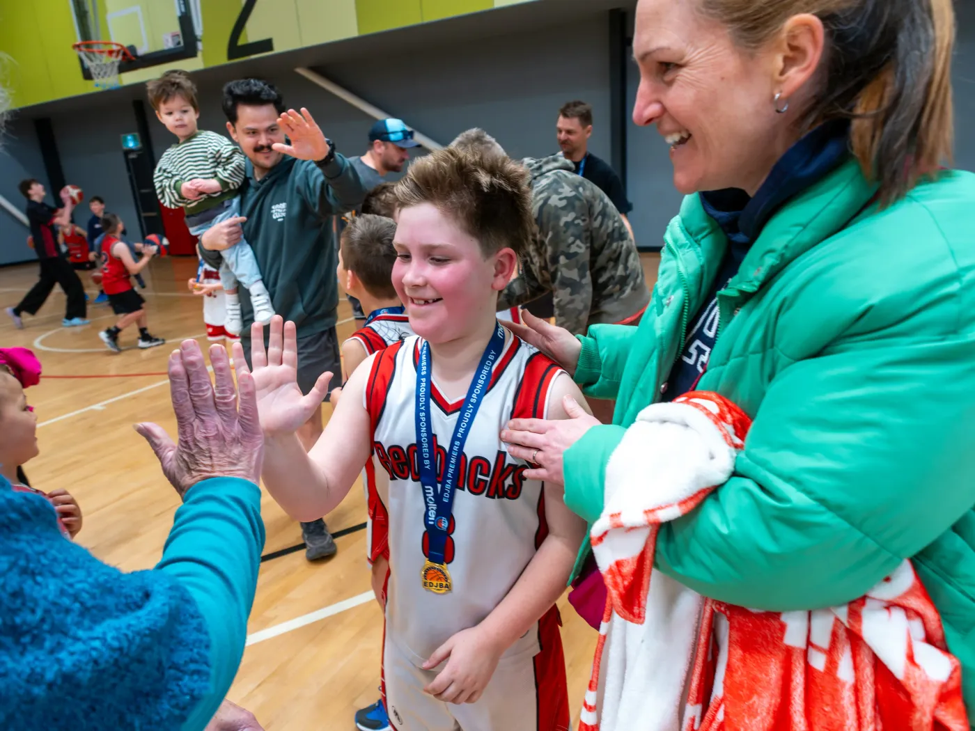 A young Redback with a grand final medal high-fiving family in the crowd