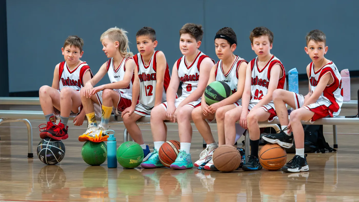 A Redbacks junior team sitting along the bench with their basketballs
